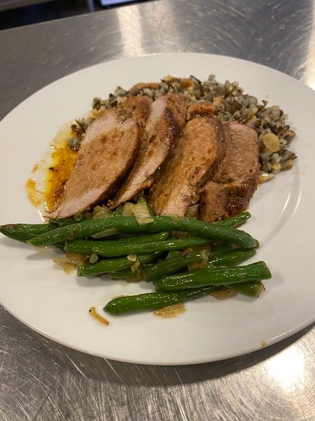 A white plate topped with meat and green beans on a table.