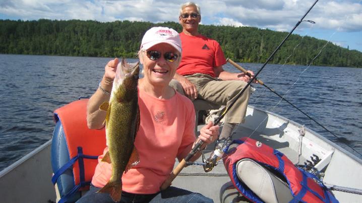 Woman in a boat holds up a walleye fish she caught.