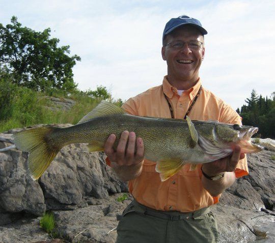 A man smiling as he holds up with walleye caught at Oak Lake Lodge and Outpost.