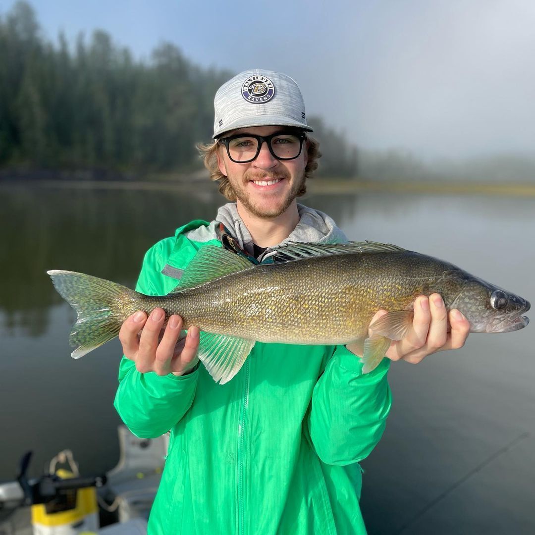 Young Zachary holding up his large walleye fish he caught under blue skies.