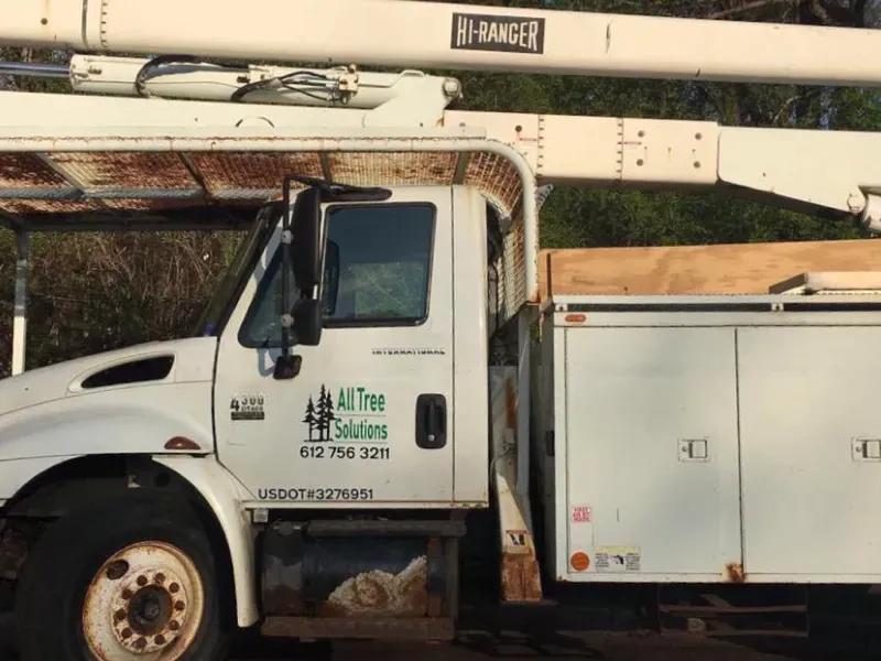 A white all tree solutions truck is parked on the side of the road