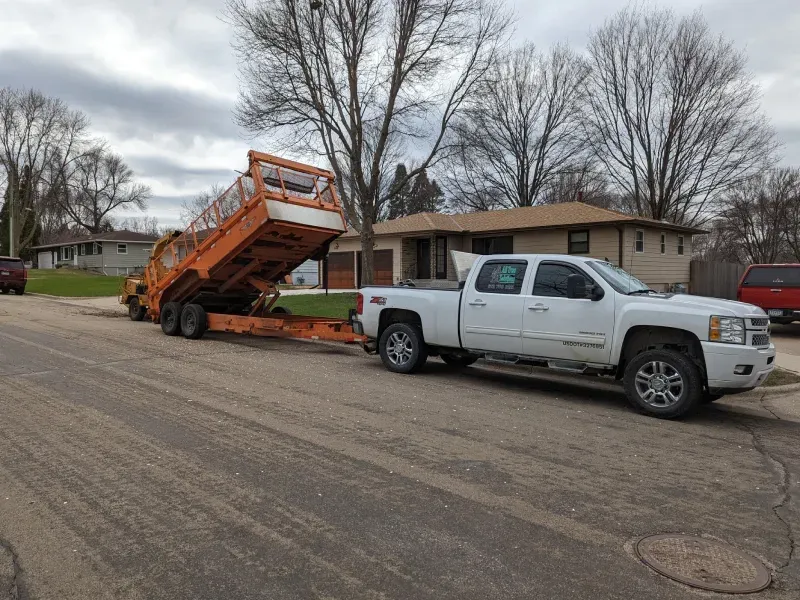A white truck is towing a dump truck on a trailer.