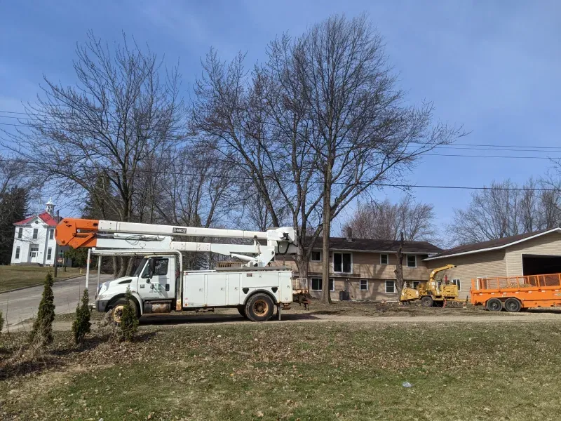 A white truck with a crane on top of it is parked in front of a house.