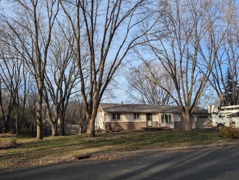 A house is surrounded by trees and a truck is parked in front of it.