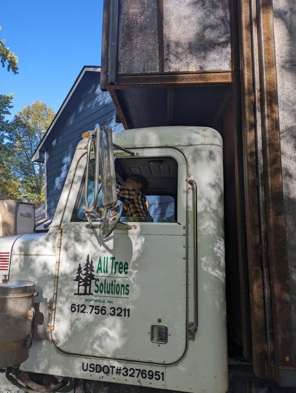 A white all tree solutions truck is parked in front of a house.