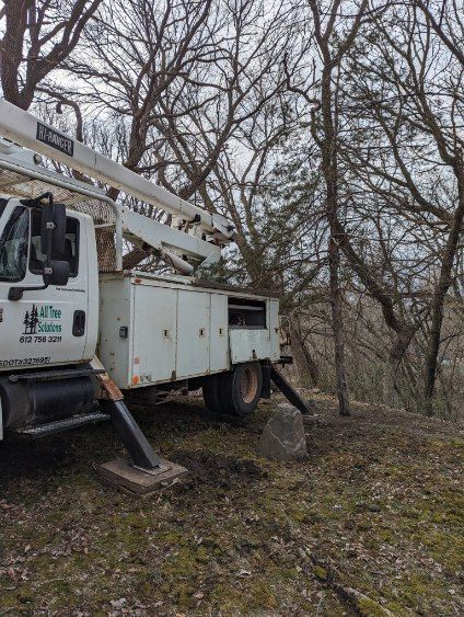 A white truck with a crane on top of it is parked in the woods.