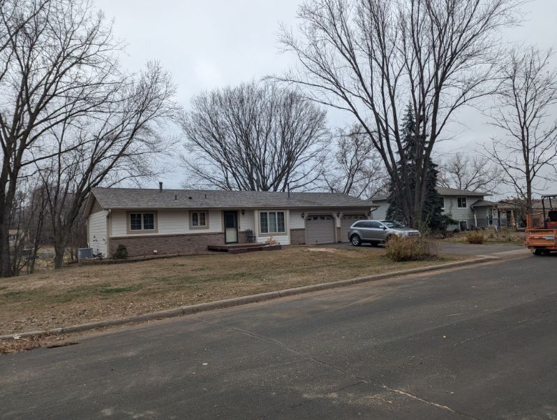 A house with a car parked in front of it and trees in the background.