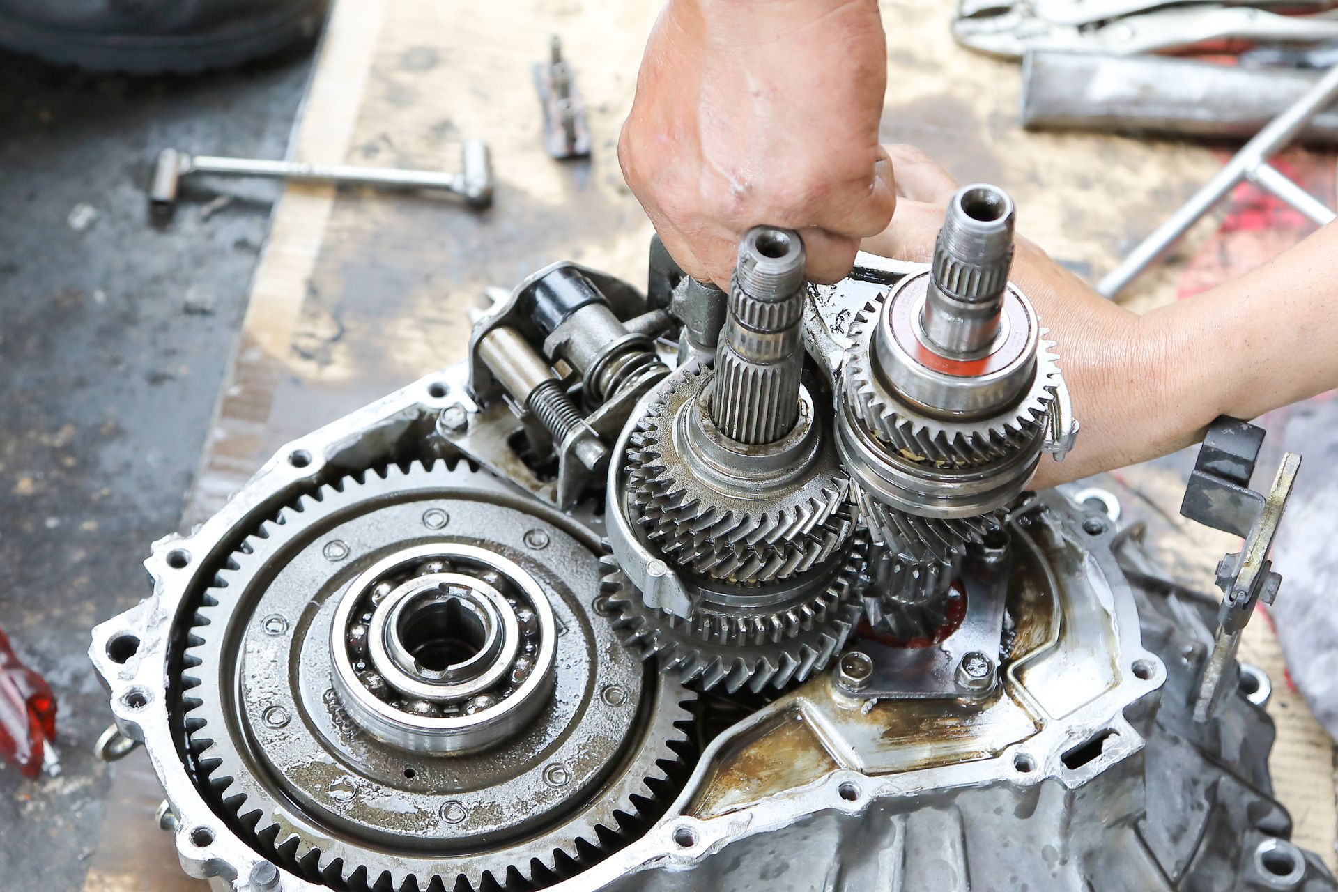 Hand working on an open car transmission with various gears and bearings visible.