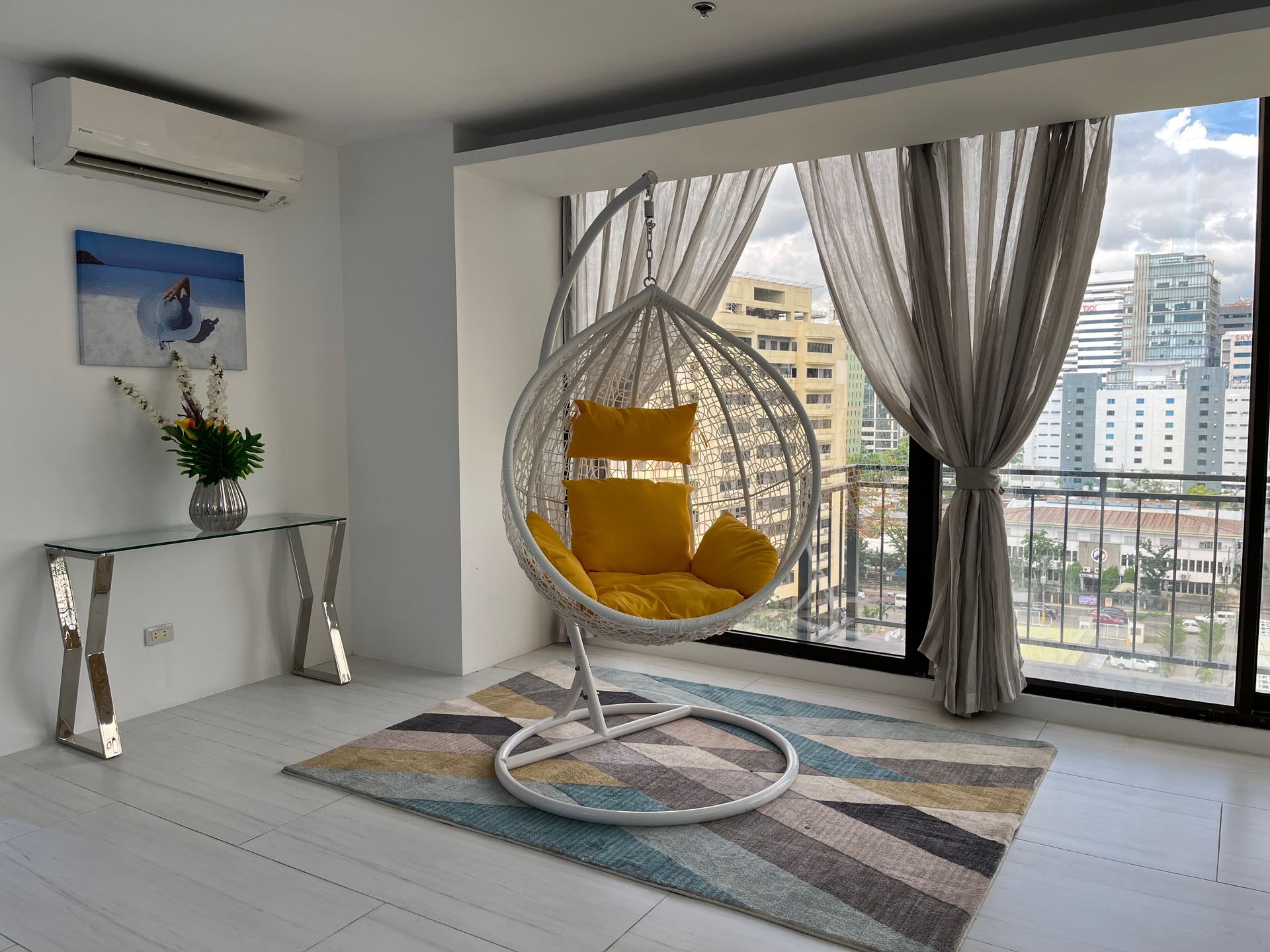 A living room with a hanging chair and a rug in front of a large window.