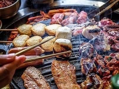 A person is holding chopsticks over a grill of meat and vegetables.