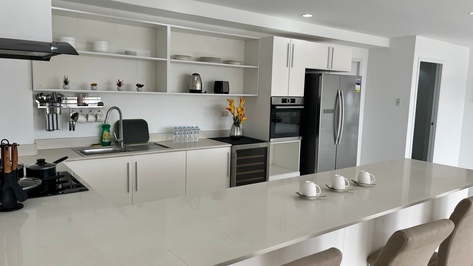 A kitchen with white cabinets , a stove , a refrigerator , a sink , and a bar.