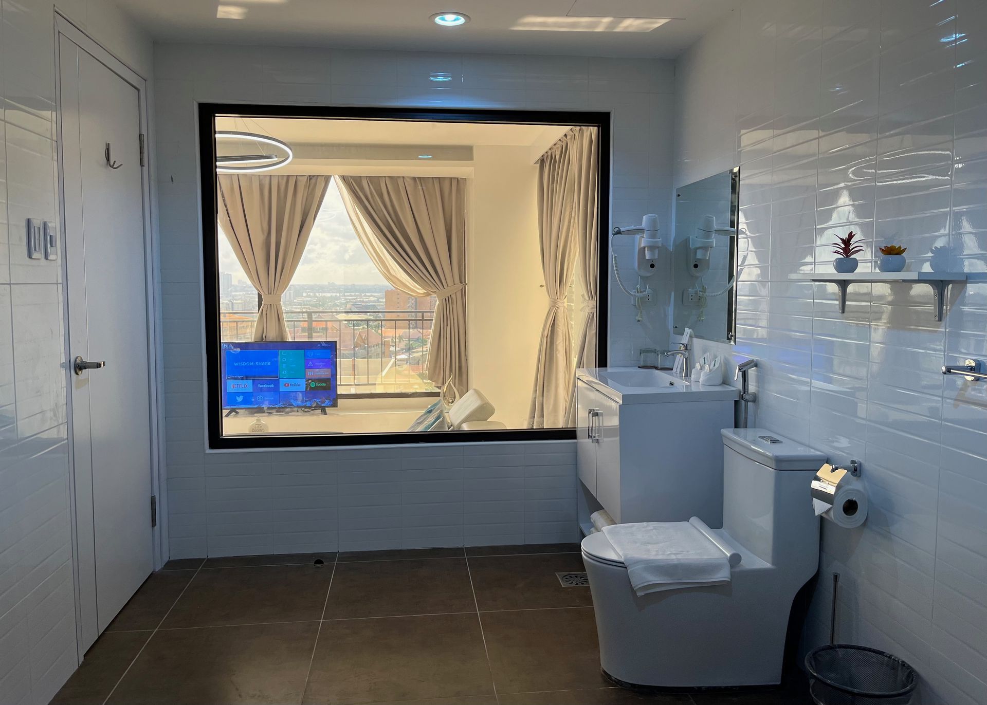 A bathroom with a toilet , sink , mirror and window.