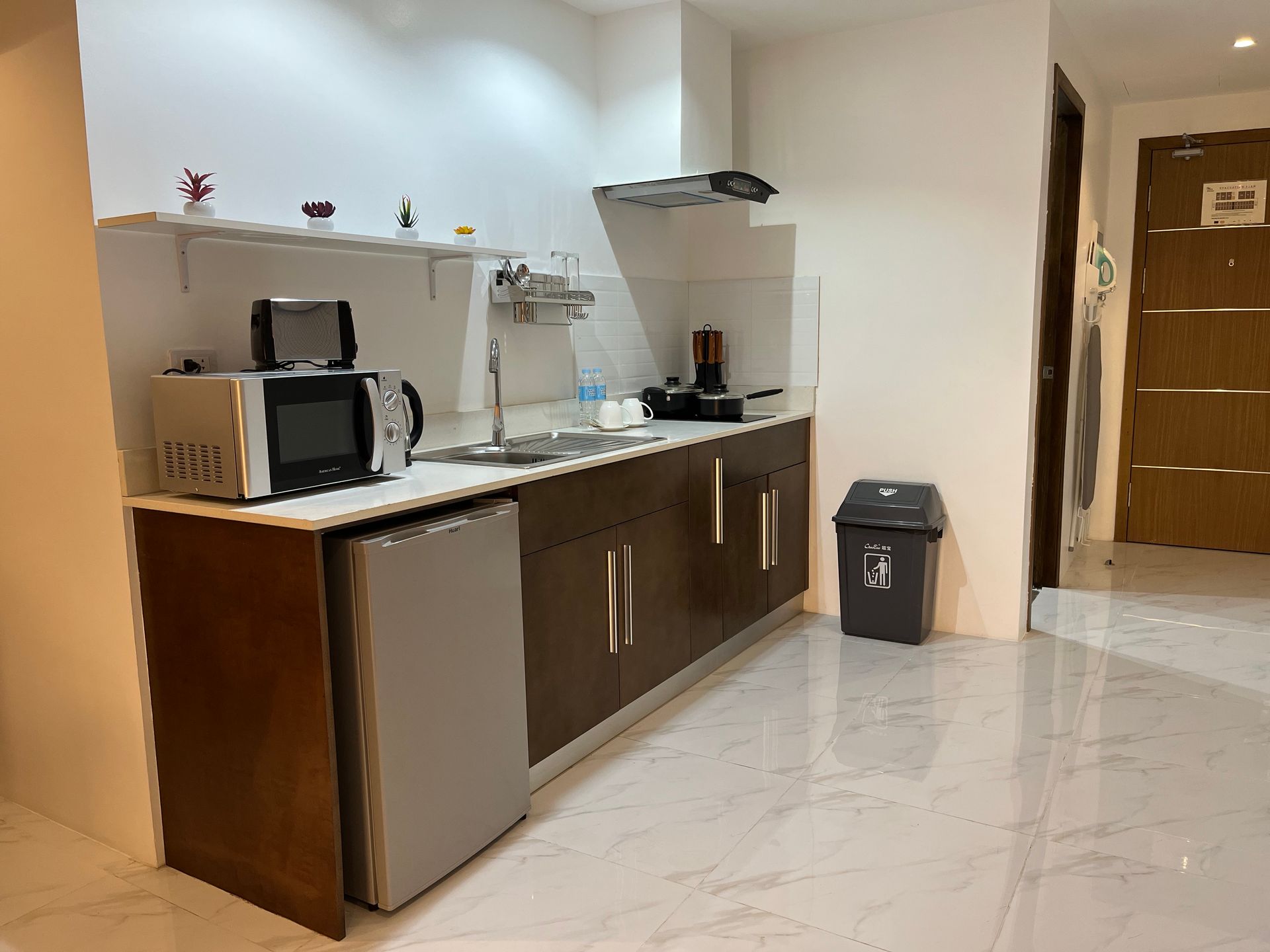 A kitchen with a sink , microwave , refrigerator and trash can