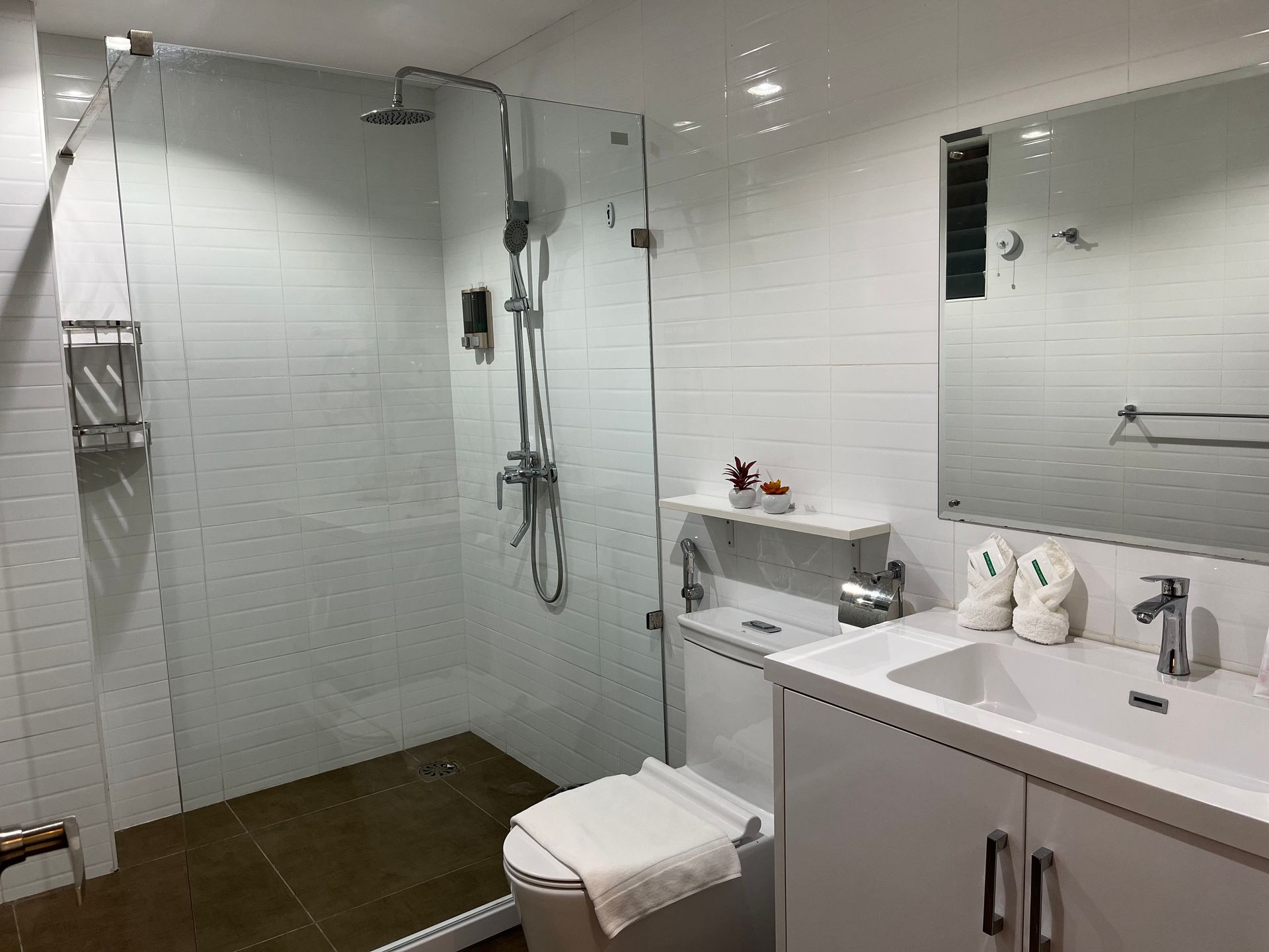 A bathroom with a toilet , sink , shower and mirror.