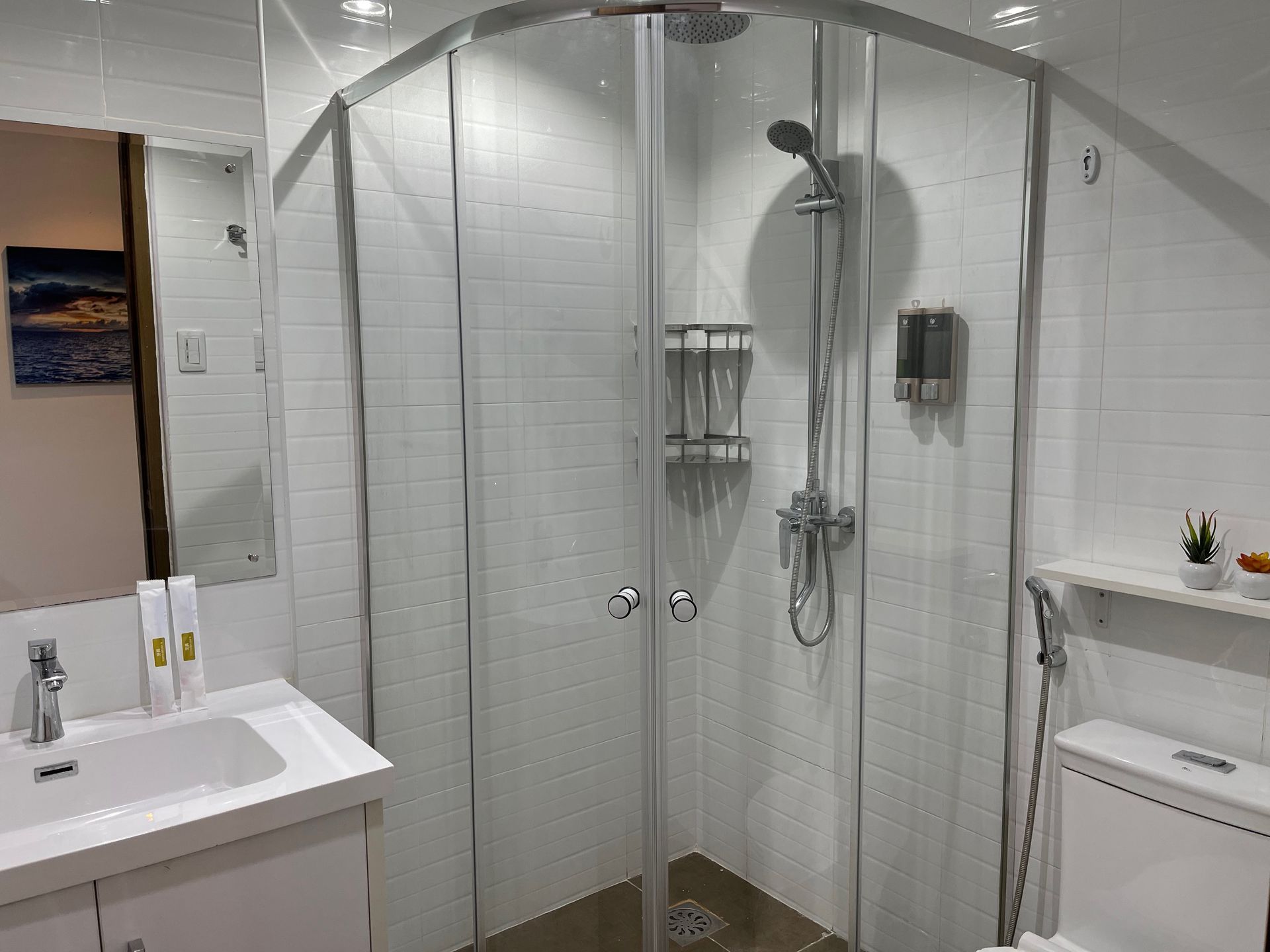 A bathroom with a shower , sink , toilet and mirror.