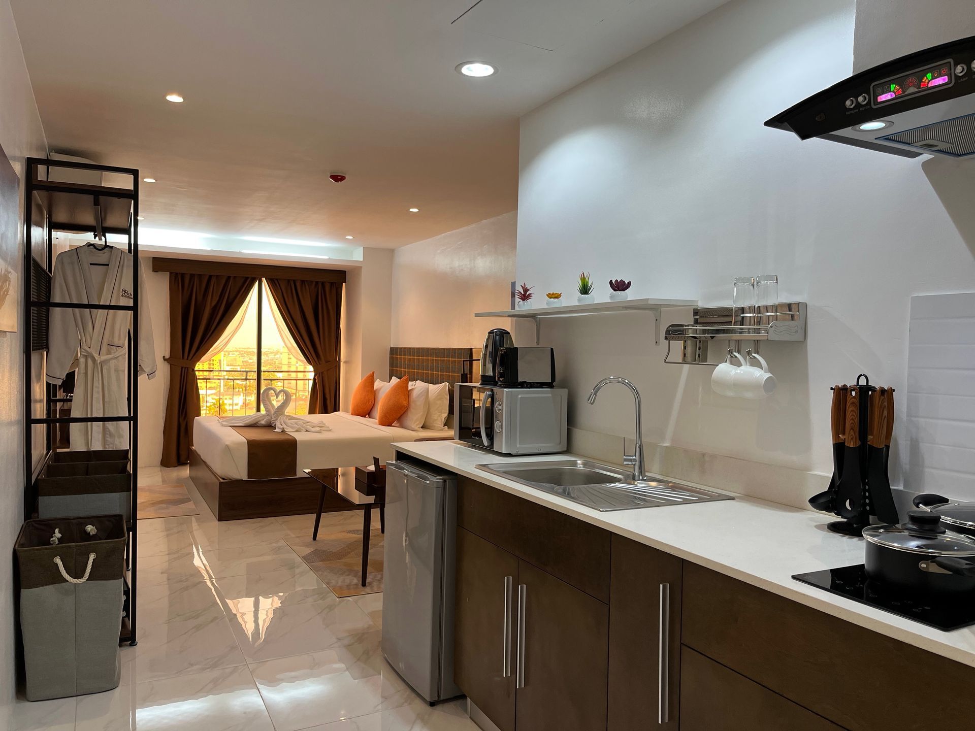 A kitchen in a hotel room with a bed in the background.