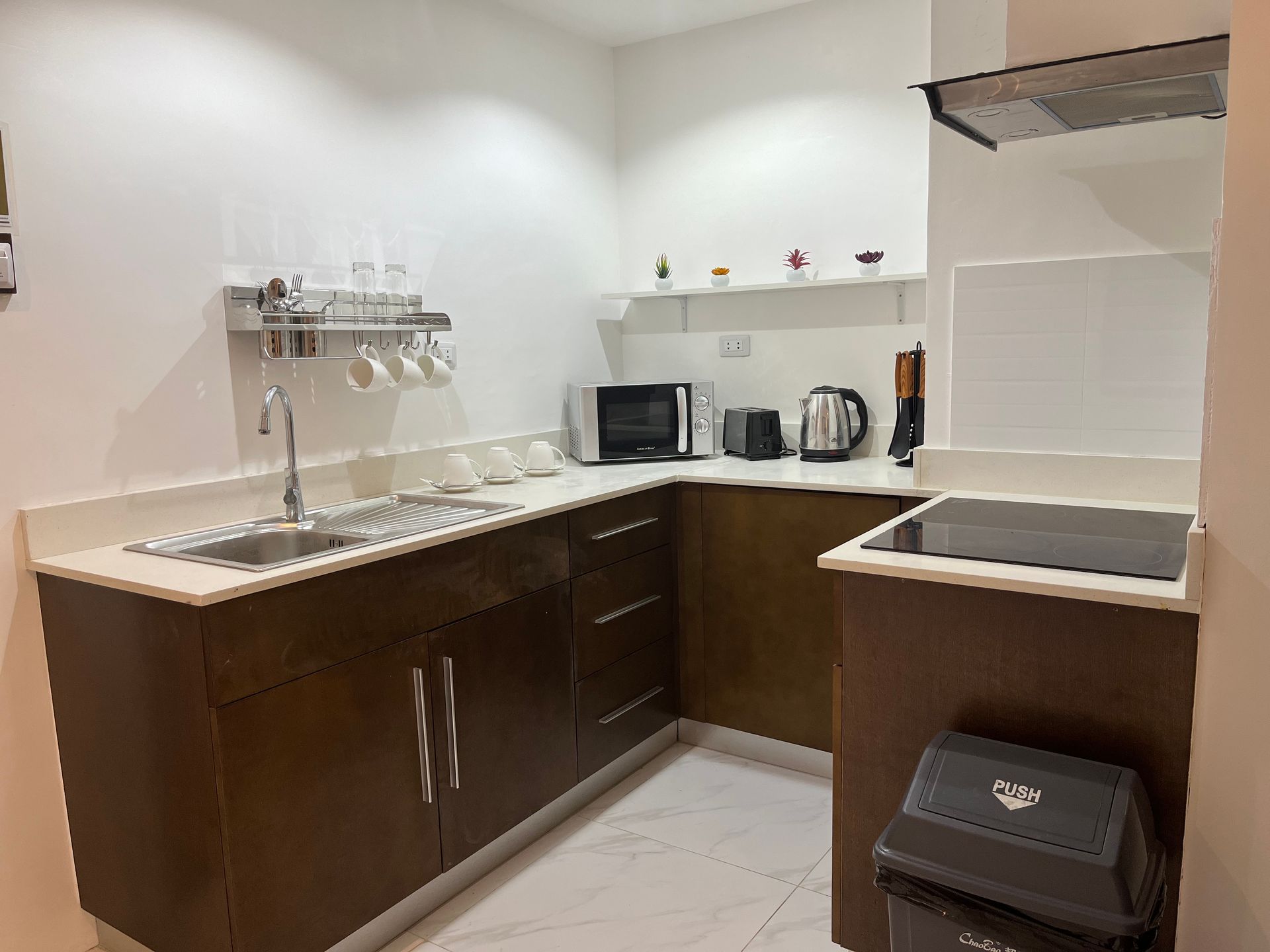 A kitchen with a sink , stove , microwave , and trash can.