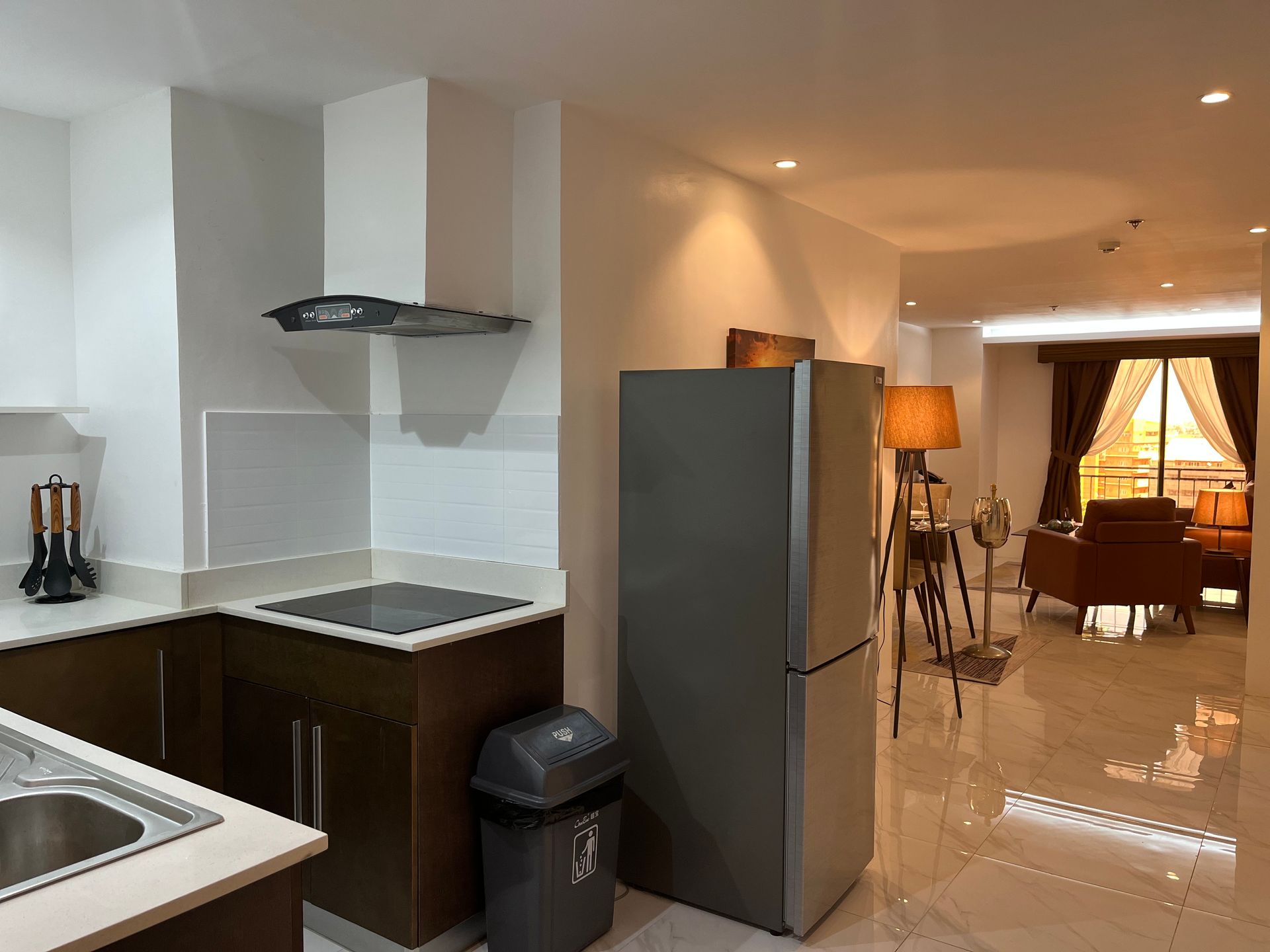 A kitchen with a refrigerator , sink , stove and trash can.