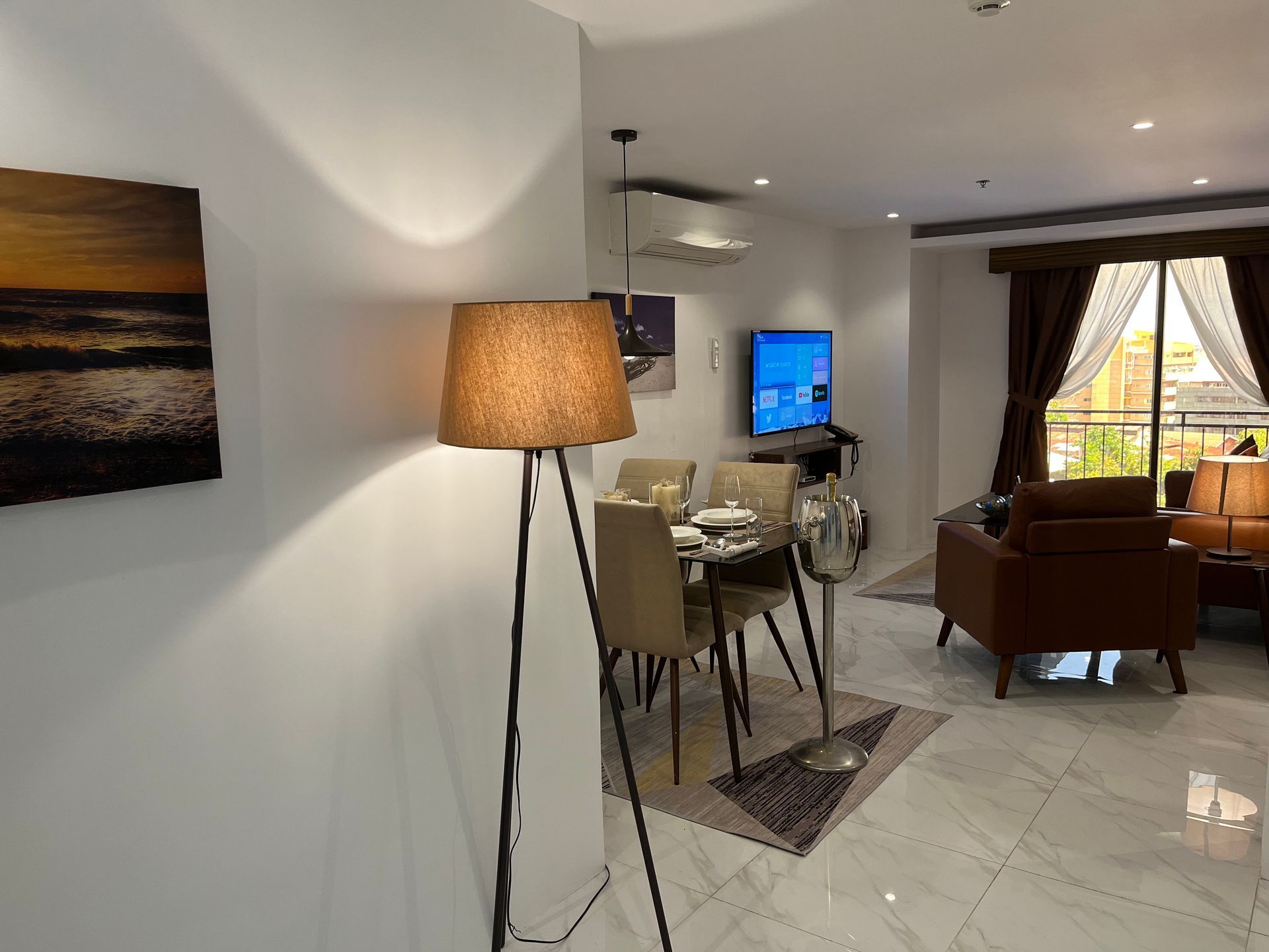 A living room with a dining table , chairs , a lamp and a television.