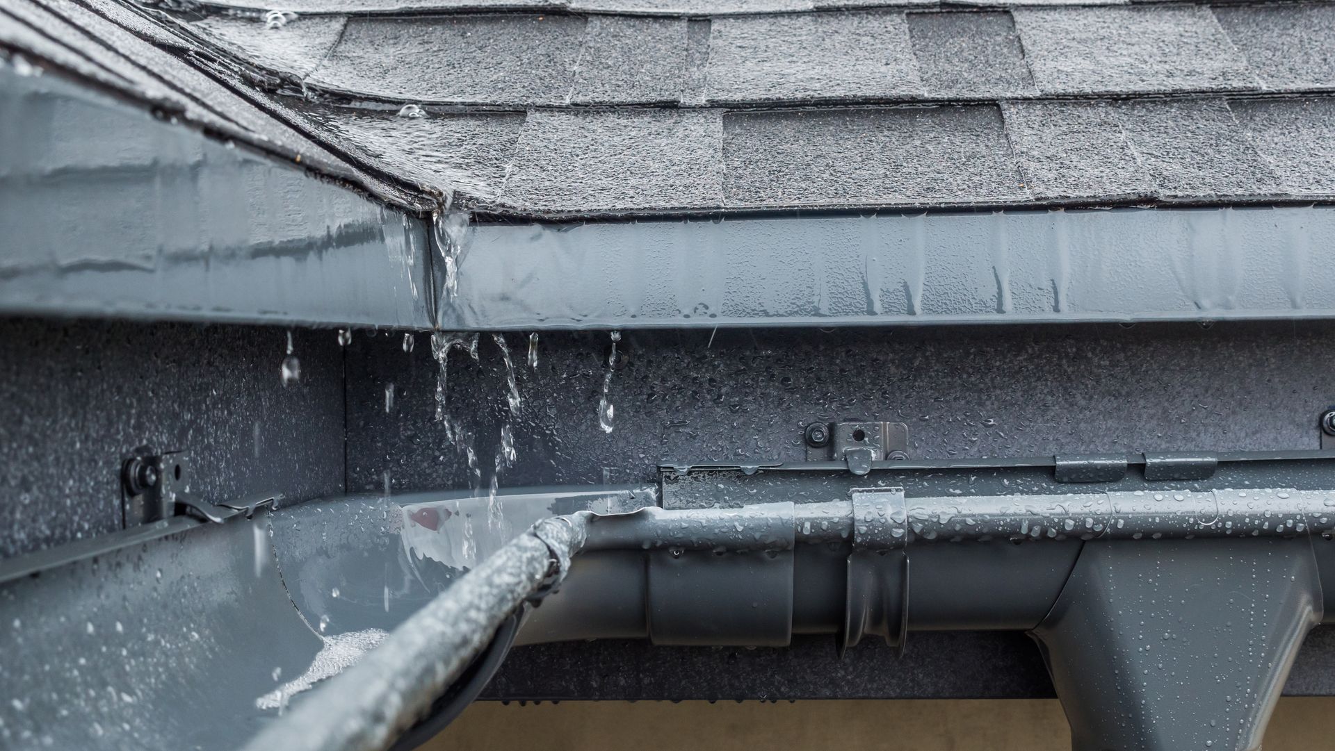 Frozen gutter with icicles and water dripping, likely from a roof in winter.