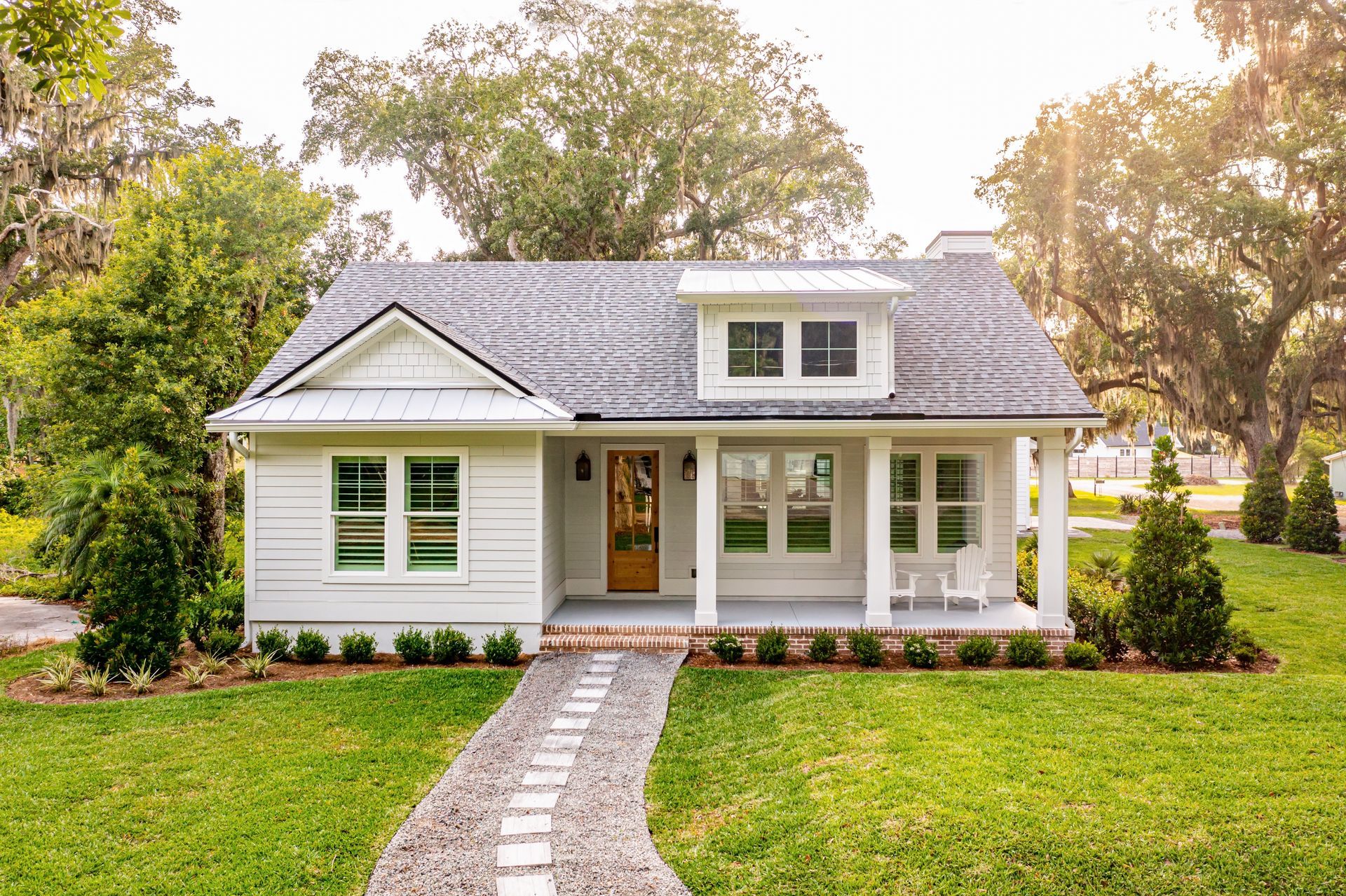 White cottage home with a stone pathway leading to the front door, surrounded by a green lawn and trees.