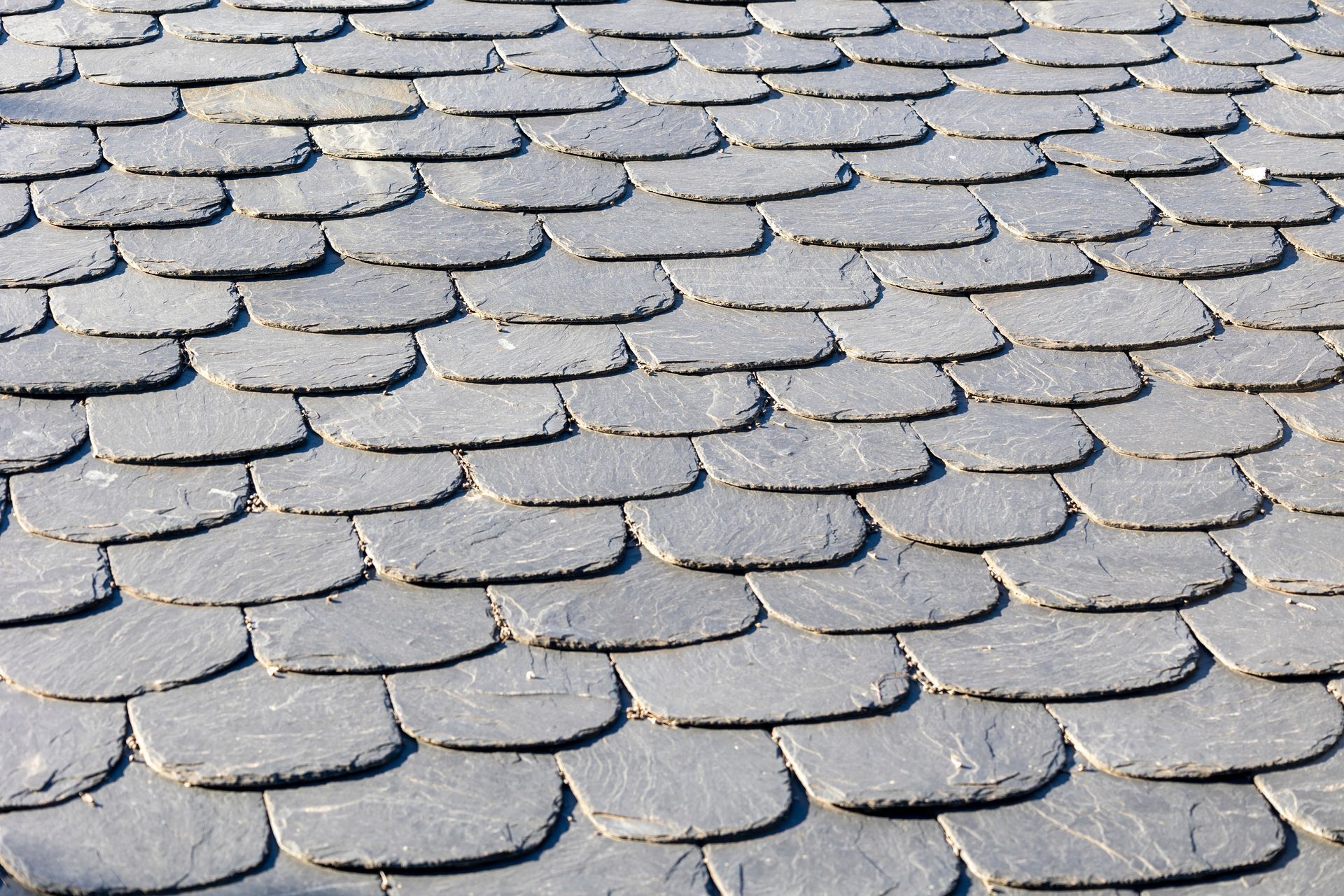 Close-up view of a roof covered in overlapping, dark gray, scale-like slate tiles.