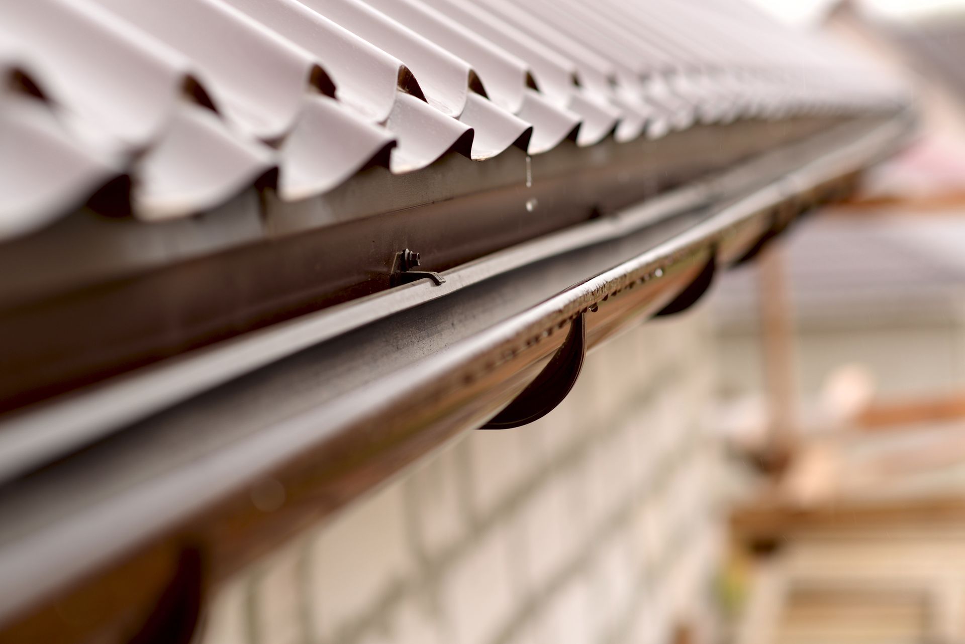 Brown roof gutter with visible rain drops, attached to a brick building.