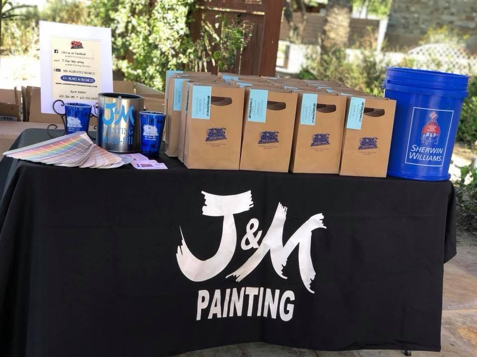 Table with J&M Painting logo, boxes, paint supplies, and blue bucket.