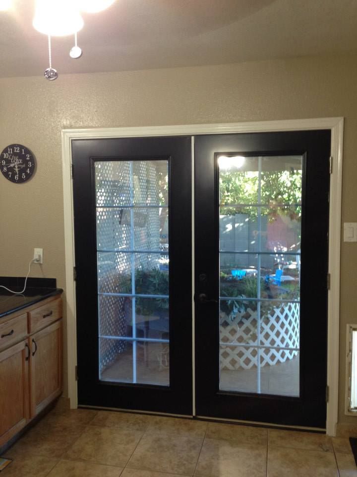 Black French doors with glass panes and white lattice outside; tan walls, light wood cabinets, and a kitchen setting.