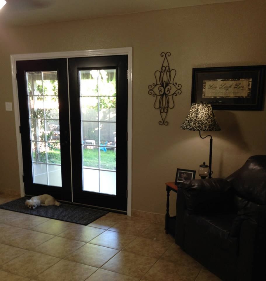 Black French doors lead to a yard. A dog rests on a mat inside. A chair and lamp are nearby.