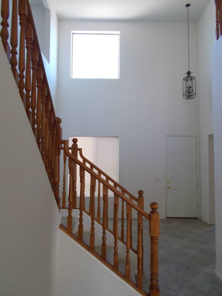 Wooden staircase with ornate railing, white walls, and a hanging light fixture.