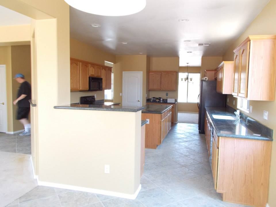 Kitchen with light-colored cabinets, dark countertops, and a man walking towards a doorway.