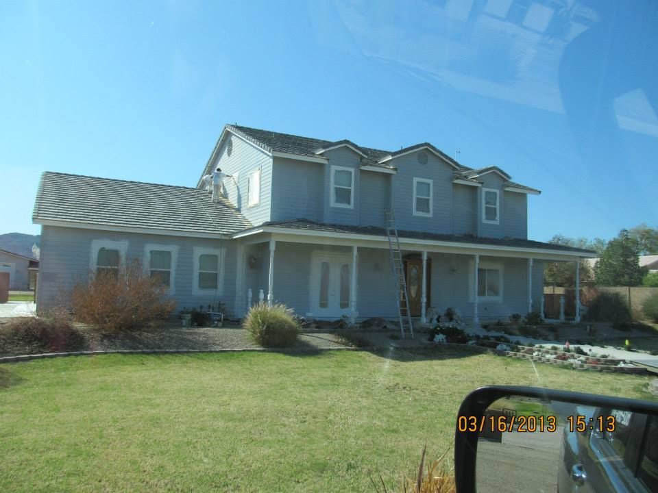 Two-story gray house with a porch, set on a green lawn under a blue sky.