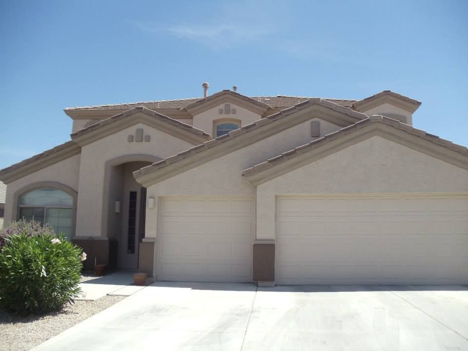 Beige two-story house with a two-car garage under a bright blue sky.
