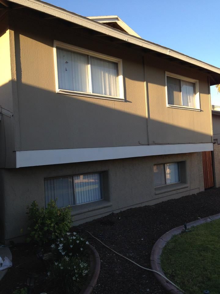 Tan two-story house with white trim. Windows are visible on both floors.  Dark mulch landscaping in front.