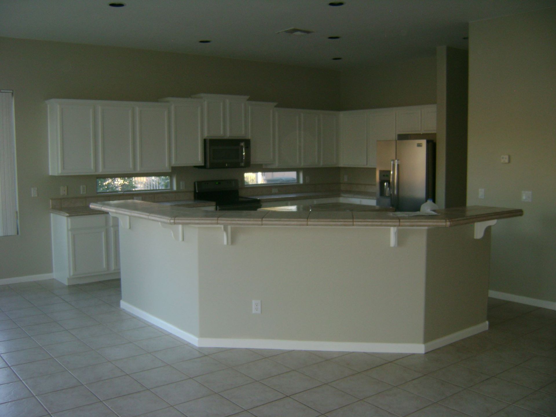 Empty kitchen with white cabinets, beige walls, and a large island.