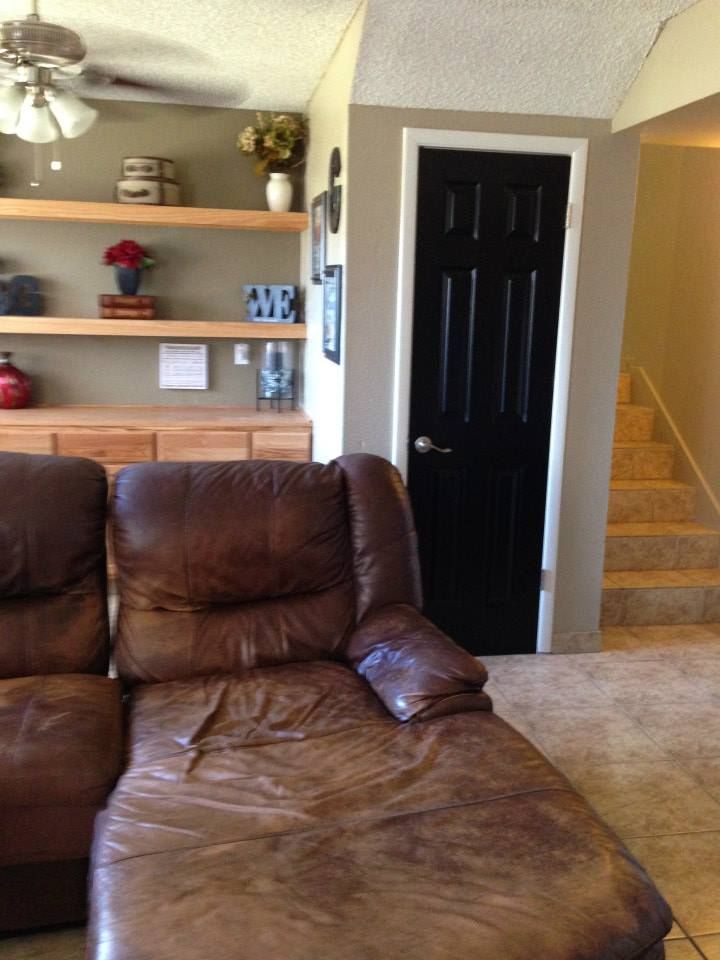 Leather couch, black door, and stairs in a living room. Brown walls and shelves with decor.