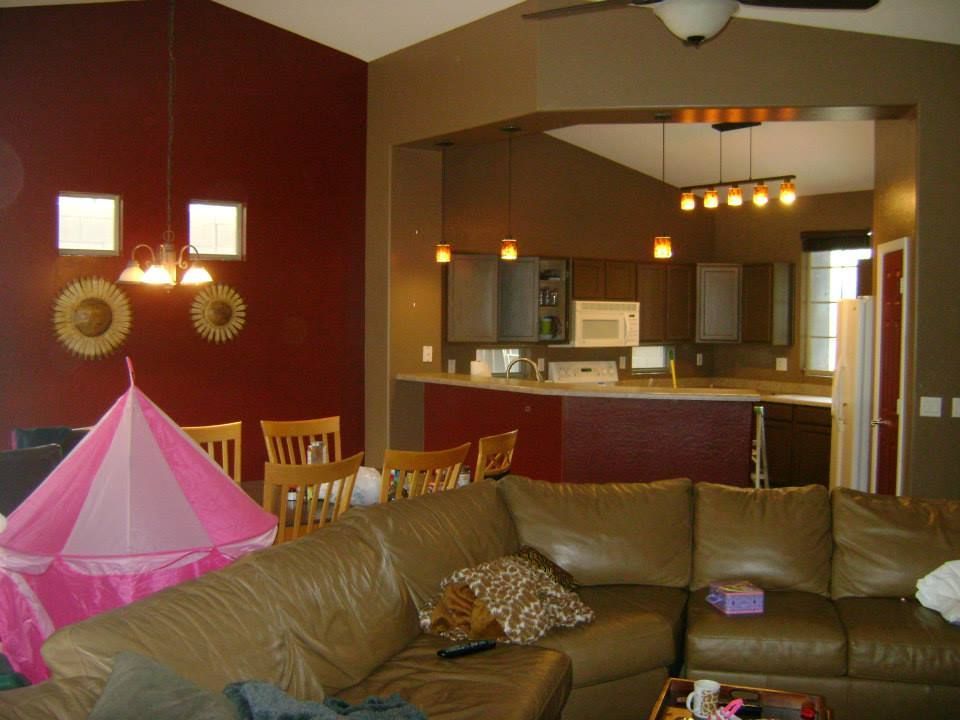 Living room with burgundy wall, leather sofa, open to a kitchen with brown cabinets.
