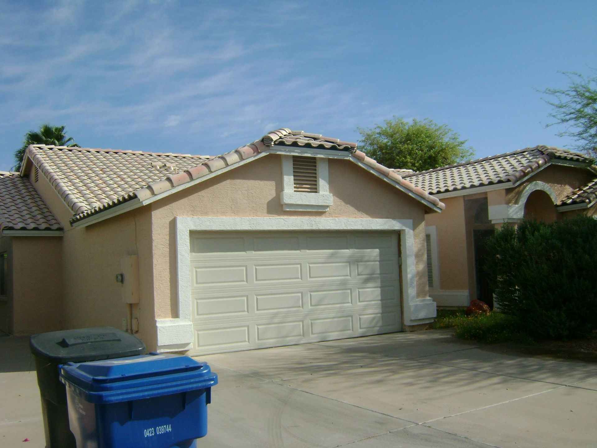 Beige stucco house with a garage, blue and black trash bins in front.