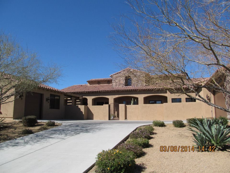 Tan stucco house with red tile roof and a concrete driveway against a clear blue sky.