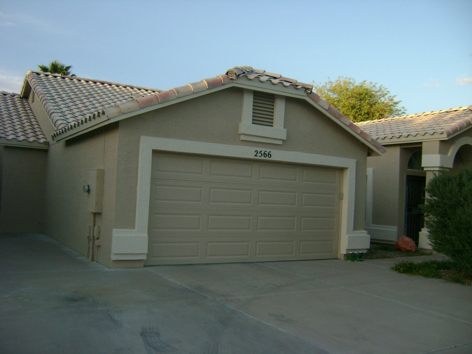 Tan stucco house with a two-car garage and a beige garage door. The roof has white tiles.