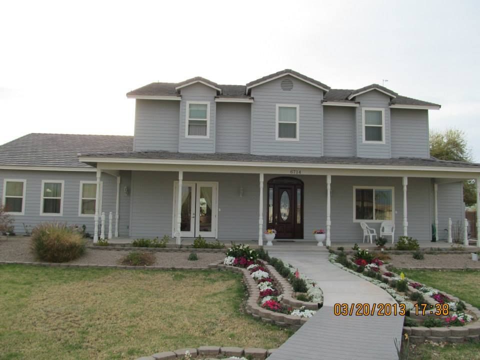 Two-story gray house with a porch and walkway lined with flowers.
