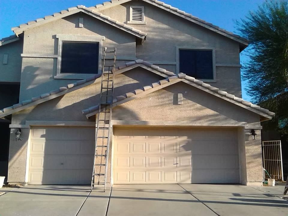 Beige two-story house with a ladder leaning against it, a sunny day.