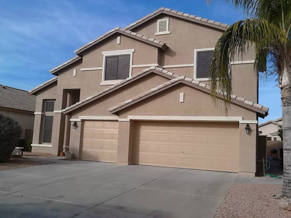 Two-story beige house with two-car garage, blue sky, and palm tree.