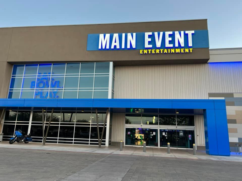 Exterior view of Main Event Entertainment, a blue and gray building with large windows.