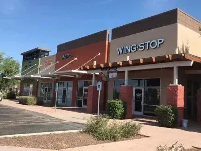 Exterior of a strip mall featuring Wingstop and other businesses on a sunny day.