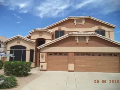 Two-story beige house with a two-car garage, tan trim, and a blue sky backdrop.
