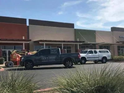 Two pickup trucks parked in front of a strip mall with a boom lift. Green, brown, and tan buildings.