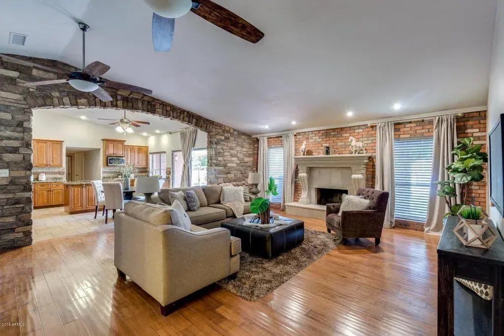 Spacious living room with stone archway and fireplace; light brown hardwood floors; neutral-toned furniture.