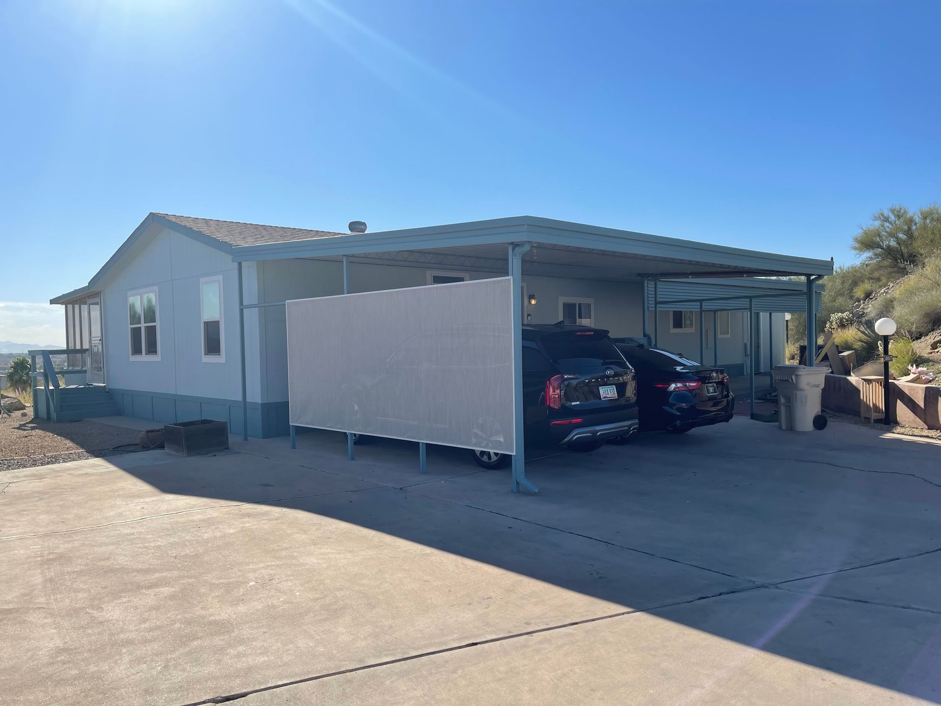 Light blue manufactured home with a carport; two cars parked. Sunny day.